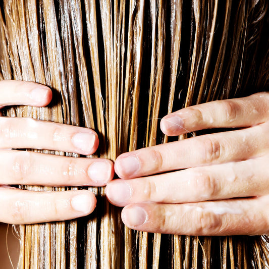 A woman applying conditioner to the full lengths of her hair