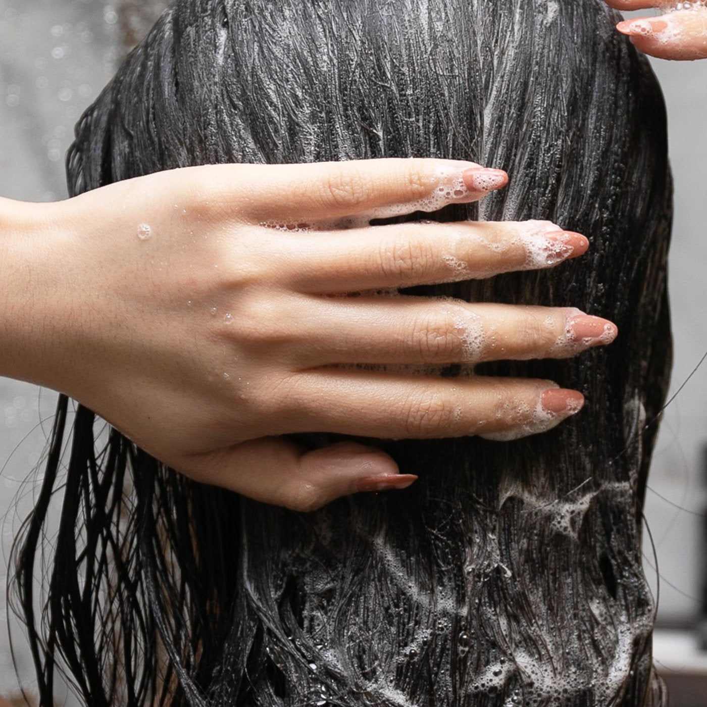 A woman lathering her hair with shampoo in the shower