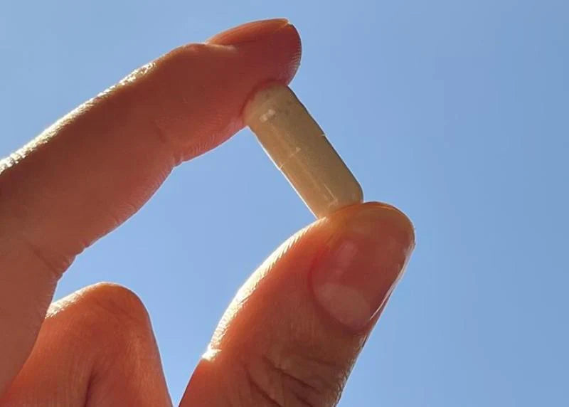 A man holding up a single supplement (let their be hair) between his fingers